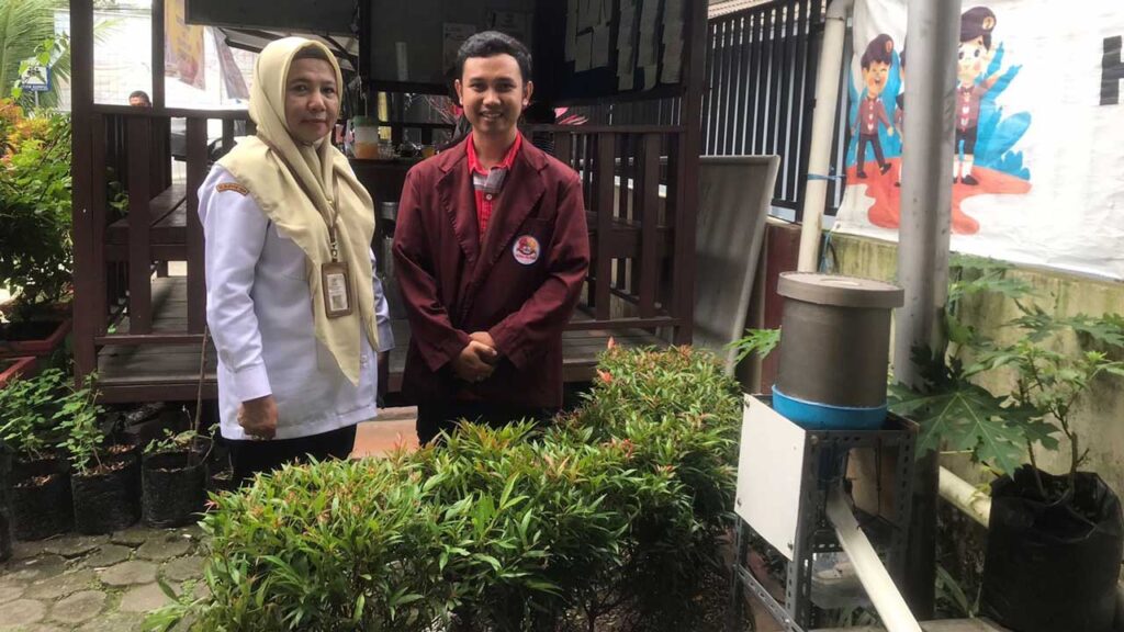 Sekretaris Lurah Gunung Sari Ulu Ny. Erni, S.H. bersama Muhammad Dimas, mahasiswa Prodi S1 Teknologi Informasi Semester 6 dan alat pakan ikan otomatis berbasis IoT. Foto: Istimewa