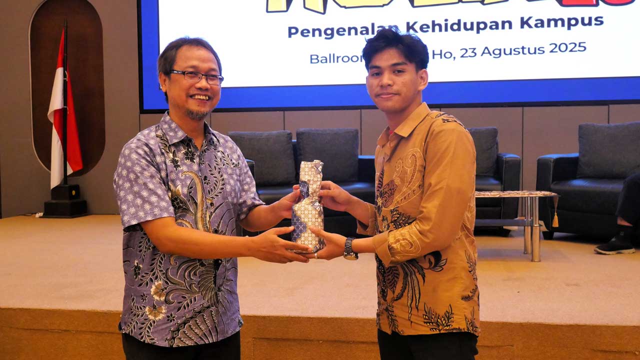 Seorang mahasiswa baru 2025 yang aktif bertanya dalam sesi paparan menerima suvenir dari narasumber Kepala Lab FIKOM, Subur Anugerah. Foto: Media Kreatif
